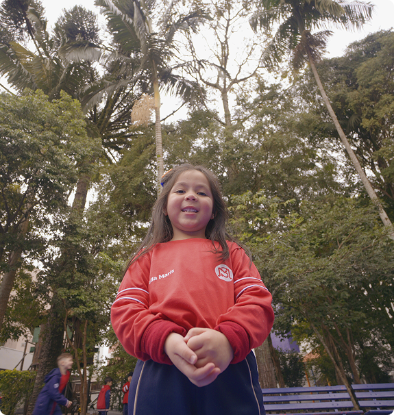 Aluna do Colégio Stella Maris sorrindo ao ar livre, cercada de árvores